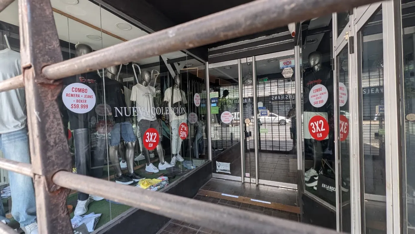 Vidriera de local de ropa en el centro de La Plata con cartel de liquidación por cierre y descuentos del 50%.